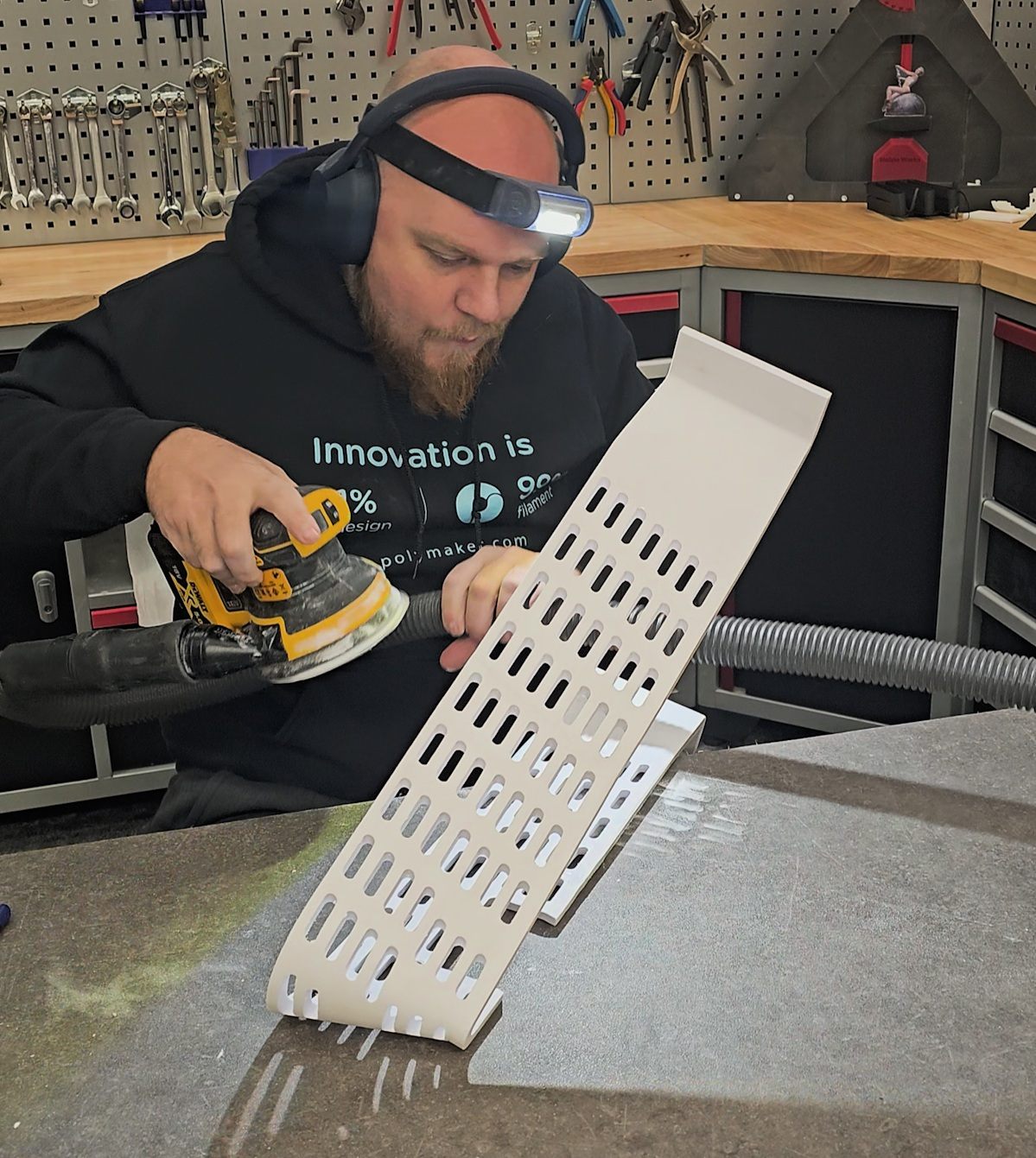 Yves sanding a printed white panel with an orbital sander in the workshop