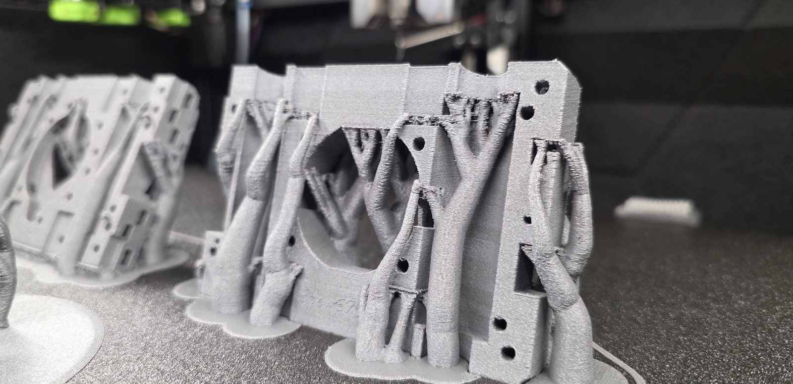 A batch of grey PPS-GF parts on the print bed, tree supports still attached, straight off the printer