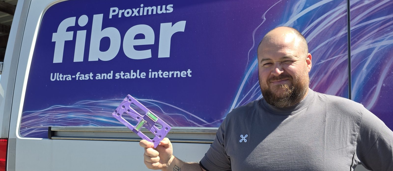 Client holding the printed installation jig, its two spirit levels in view, in front of his Proximus fibre van